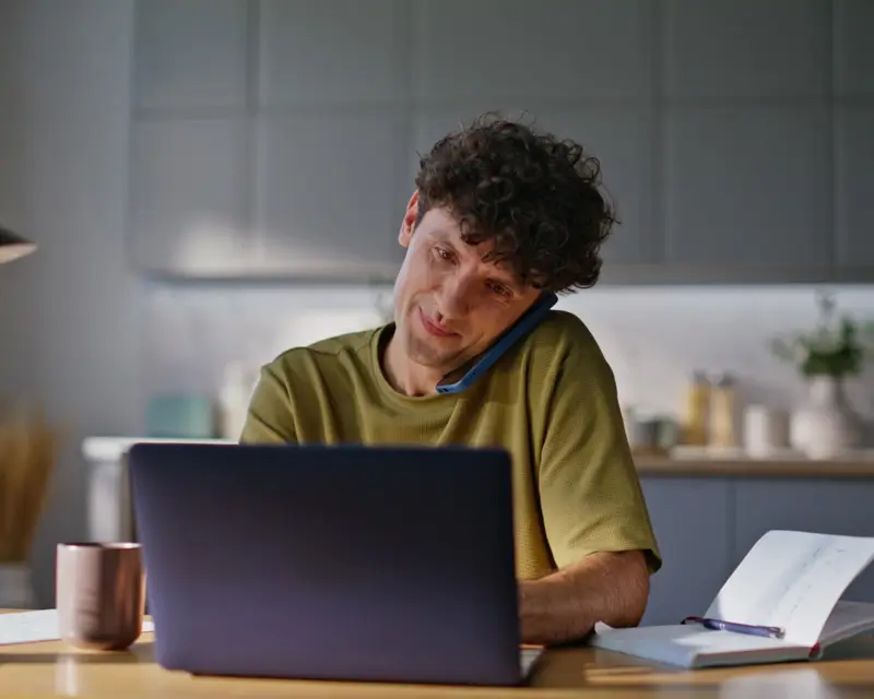 Remote worker multitasking with phone and laptop showcasing Somewhere's global talent managing recruitment operations