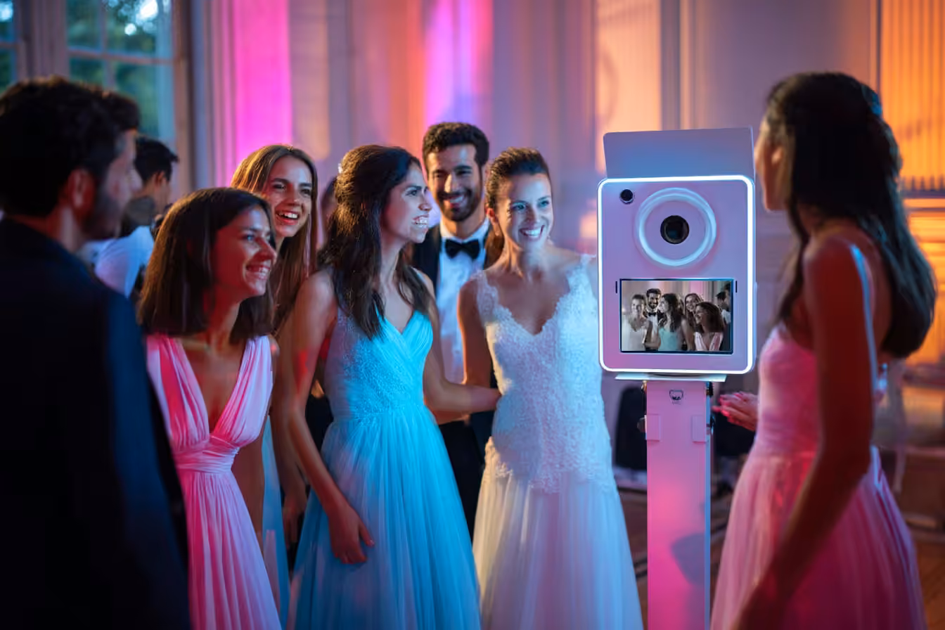 Group of friends in formal attire smiling and posing for a photo at a photo booth during a party.