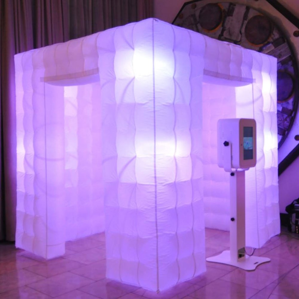 Glowing inflatable photo booth with a white touchscreen kiosk next to it on a tiled floor.