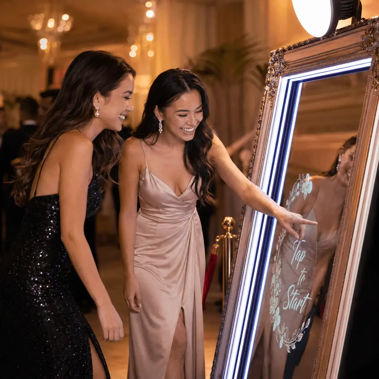 Two women using a mirror photo booth touch screen at a party