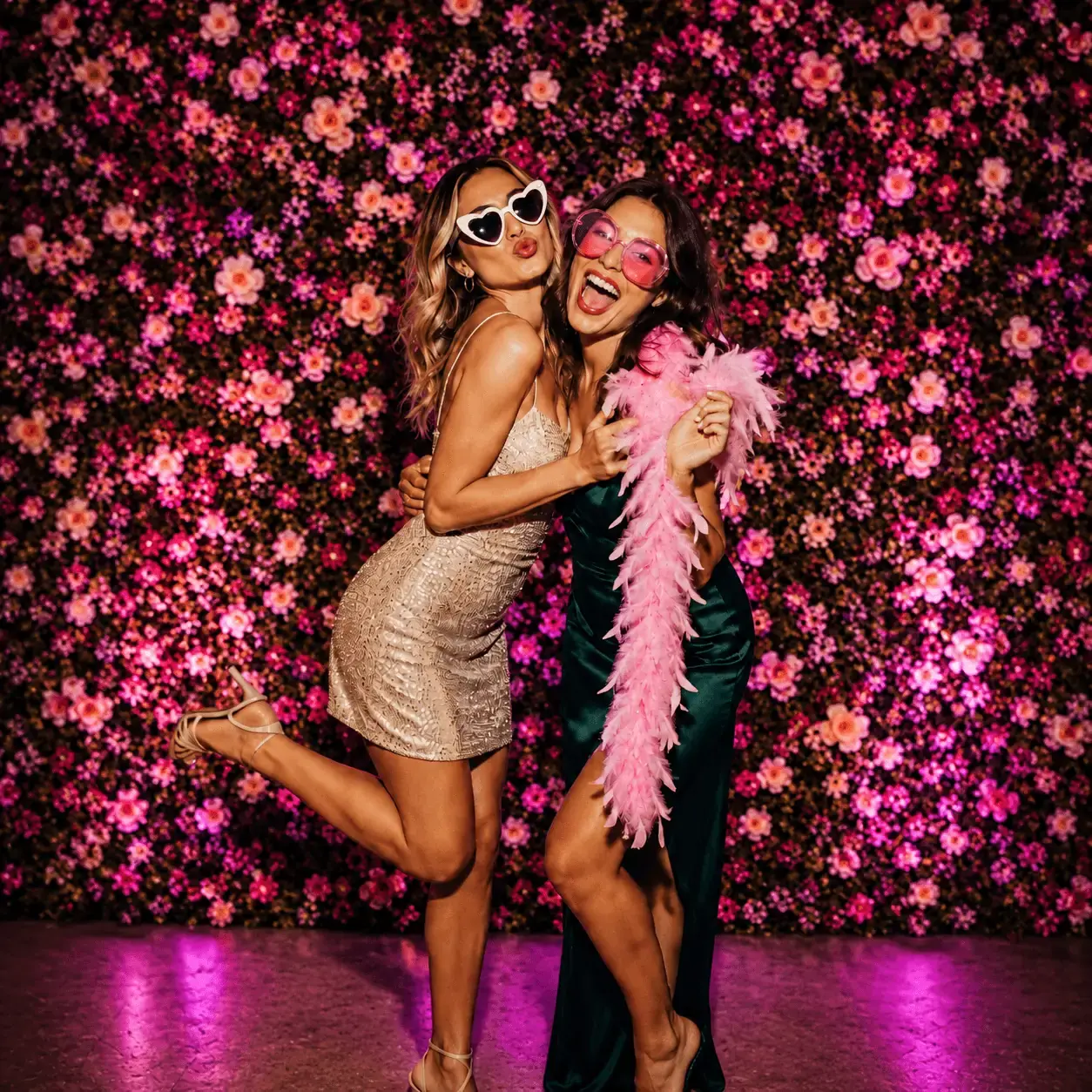 Two women posing at a floral photo booth backdrop.