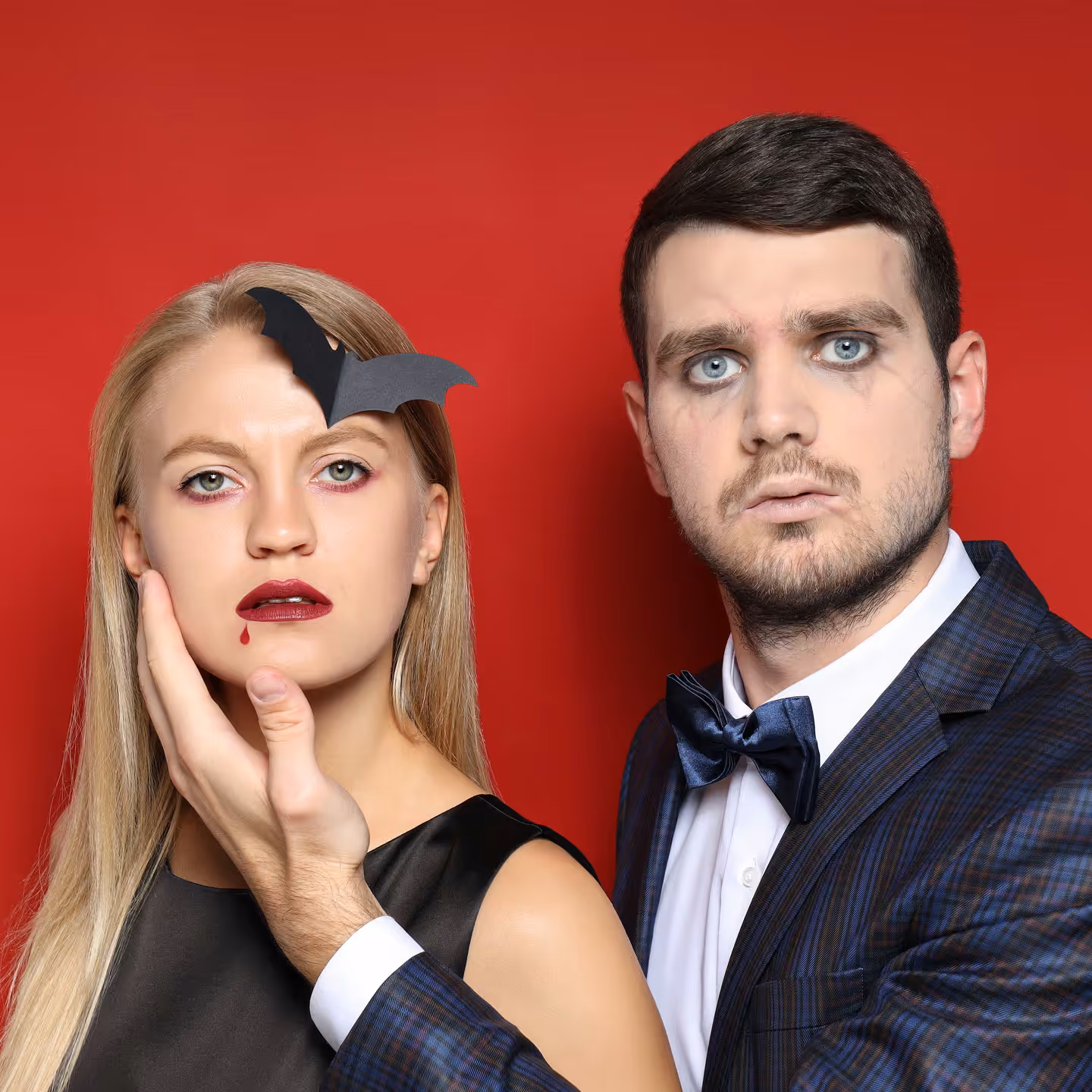 Couple in Halloween makeup posing at a photo booth against a red backdrop