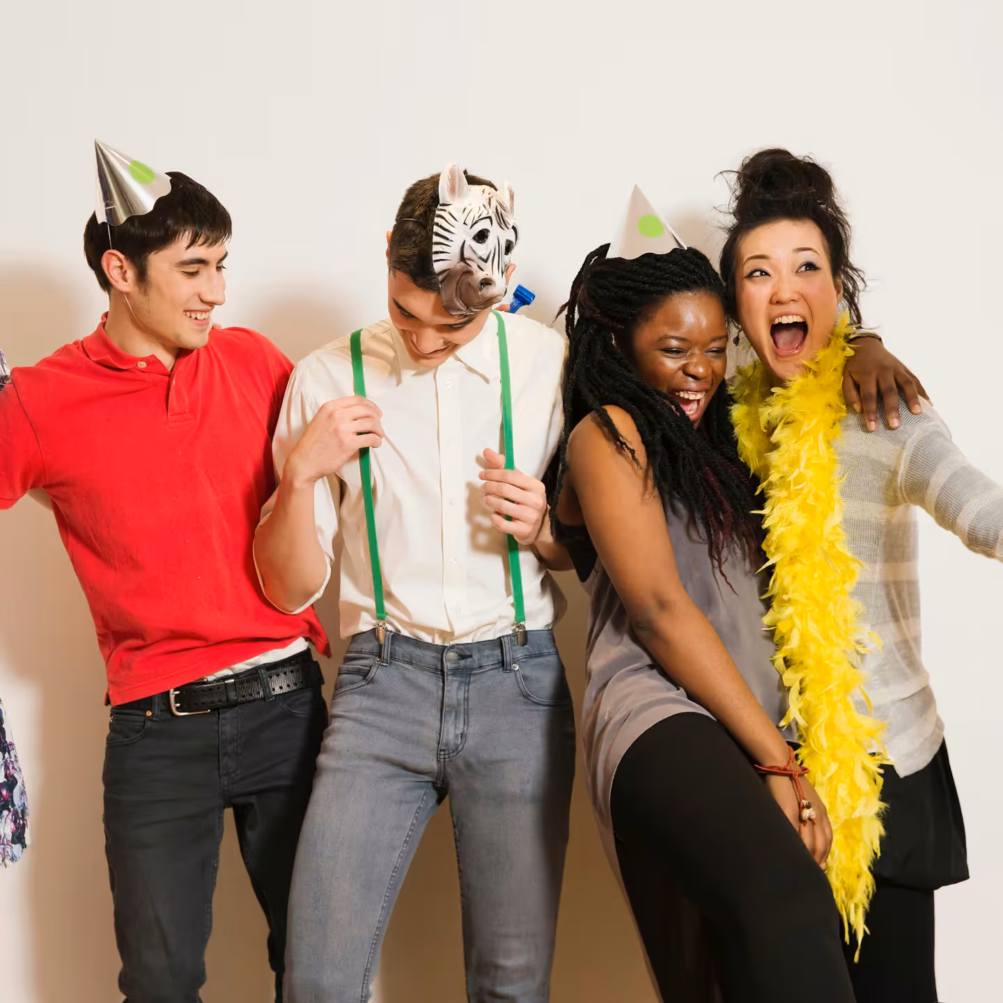 Four friends wearing party hats and accessories laughing and posing against a plain background.