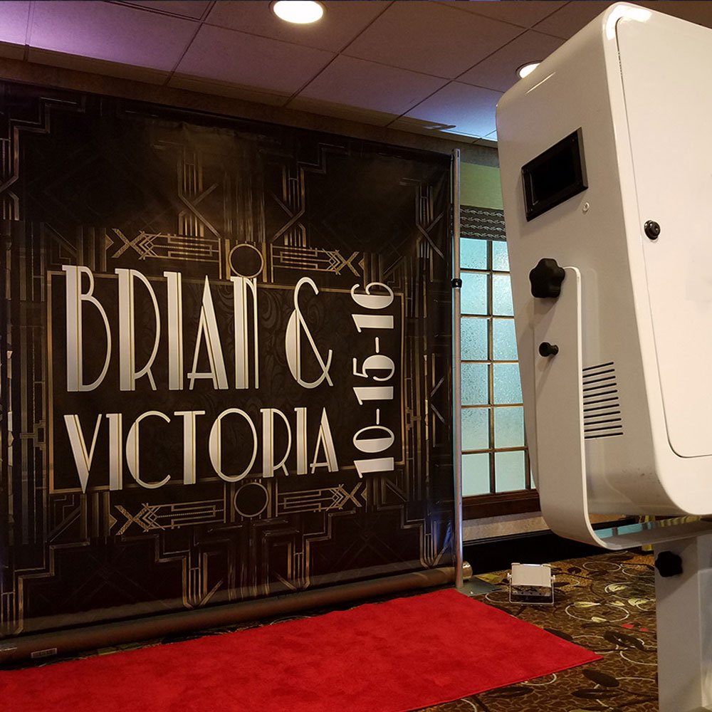 Photo booth setup with a red carpet in front of a black and gold backdrop displaying 'Brian & Victoria 10-15-16'.