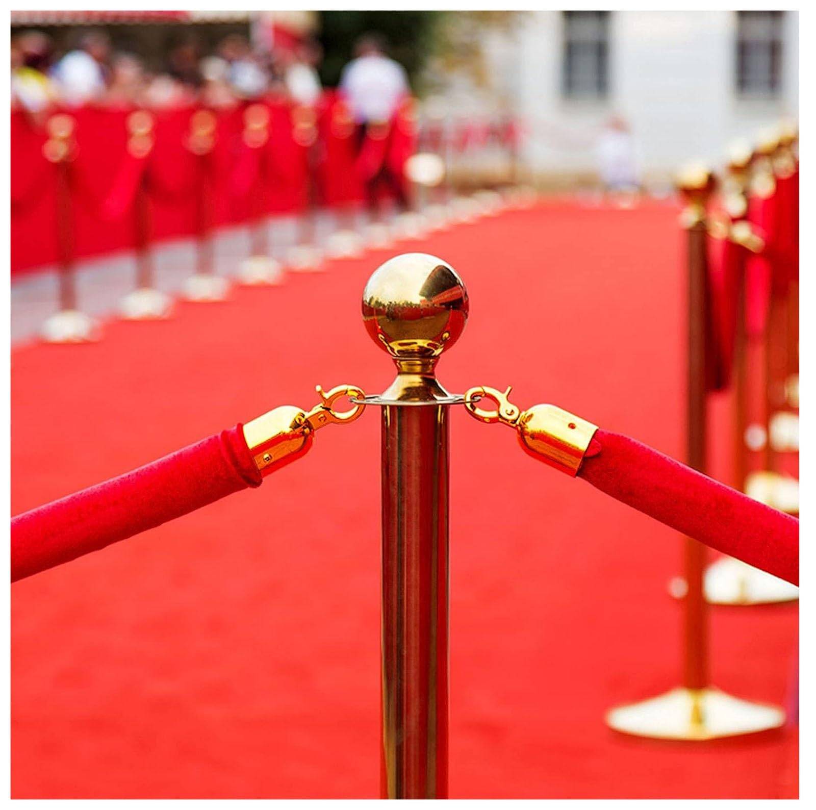 Close-up of a gold stanchion with red velvet ropes lining a red carpet entrance.