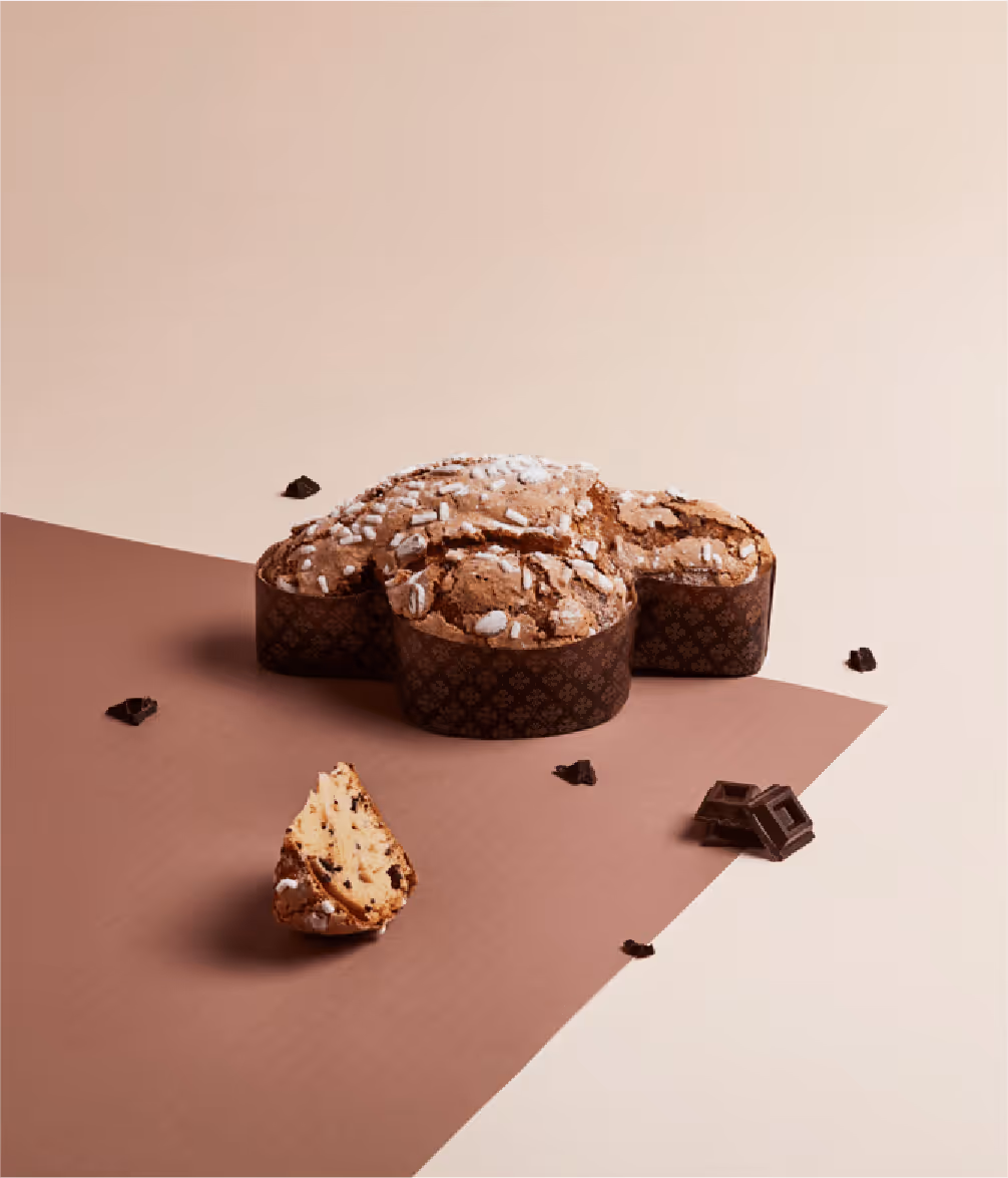 Colomba pasquale al cioccolato con glassa di zucchero e pezzi di cioccolato sparsi su sfondo bicolore marrone e beige.