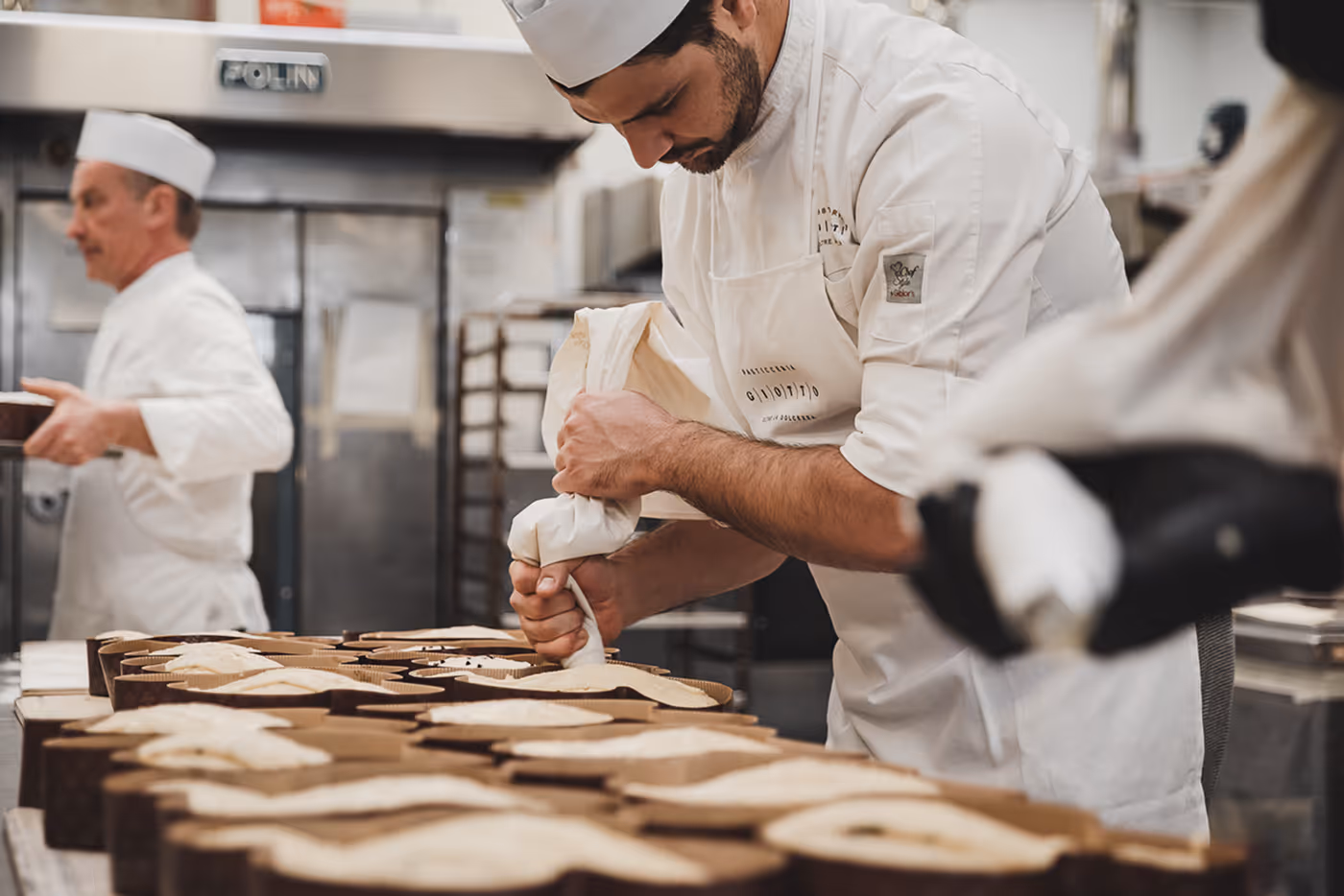 Pasticcere che riempie con una sac à poche gli stampi per dolci in una cucina professionale.