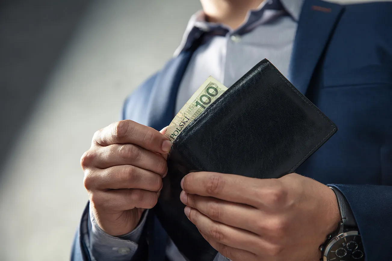 Mężczyzna chowa banknot 100 zł do portfela – oszczędności dzięki dotacji