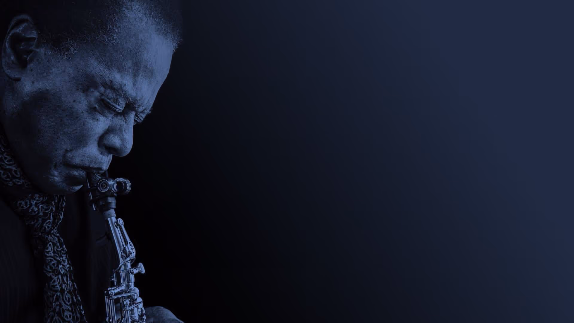 Porträt eines Mannes mit geschlossenen Augen, der leidenschaftlich Saxophon spielt vor einem dunklen Hintergrund.