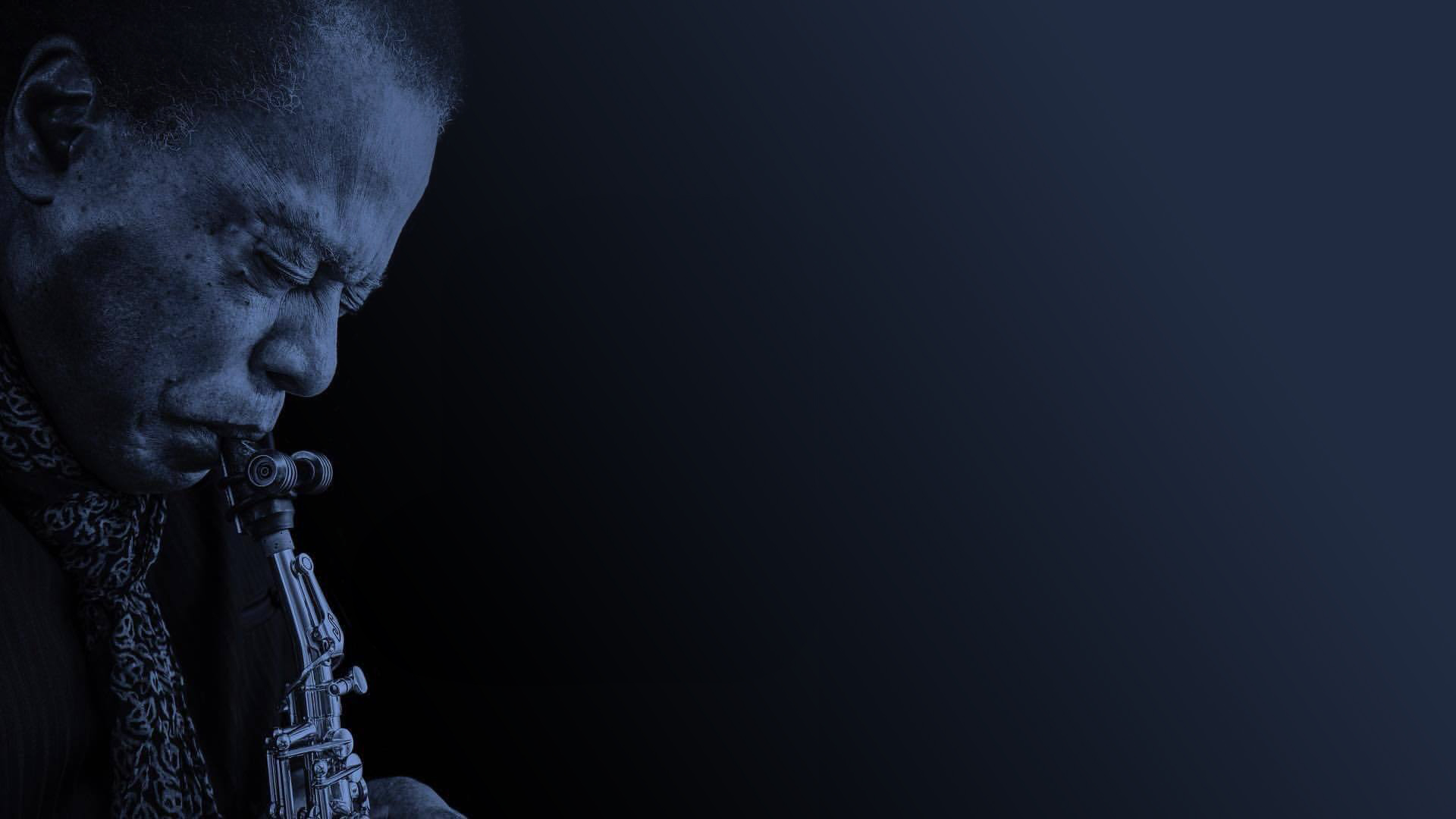 Porträt eines Mannes mit geschlossenen Augen, der leidenschaftlich Saxophon spielt vor einem dunklen Hintergrund.