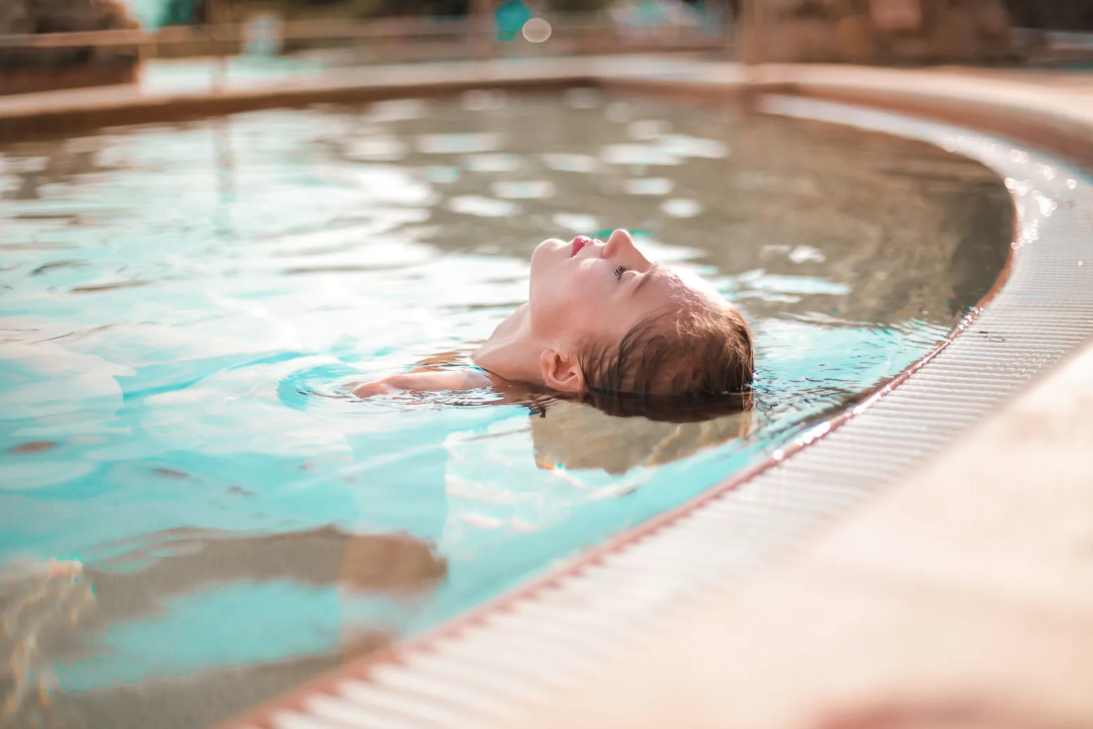 Woman floating on their back in a swimming pool with eyes closed, representing relaxation and leisure amenities at Liberty at Estrella Falls in Goodyear, AZ.