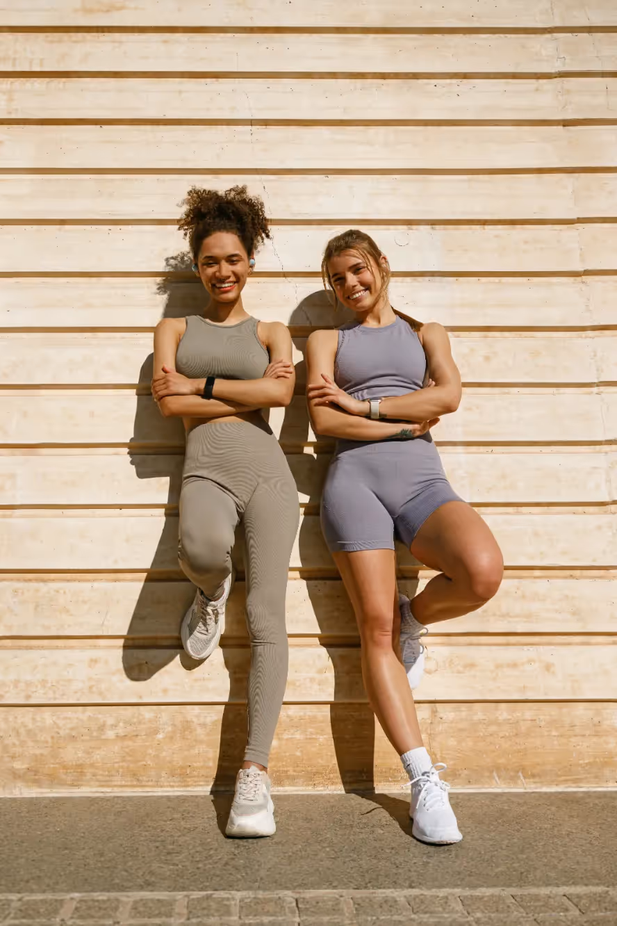 Two fit young women in athletic wear with crossed arms, smiling confidently, representing active lifestyles and fitness opportunities near Liberty at Estrella Falls in Goodyear, AZ.