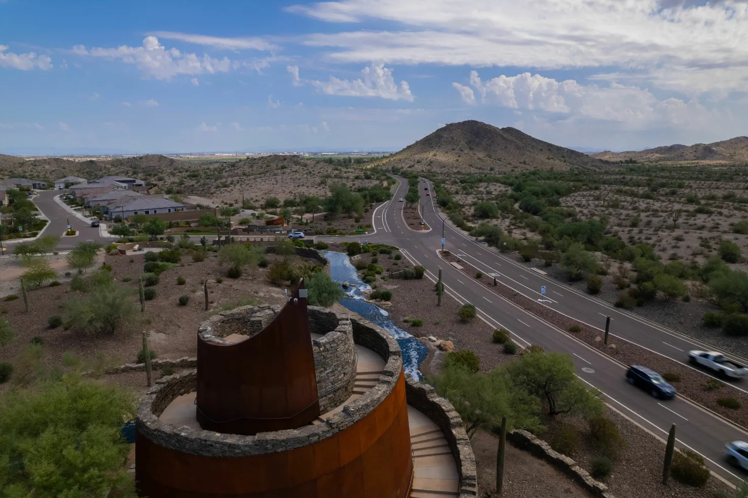 Aerial view of desert landscape estrella star tower in Goodyear, AZ, showing roads, residential areas, mountains, and a unique spiral sculpture, indicating the natural surroundings of Liberty at Estrella Falls.