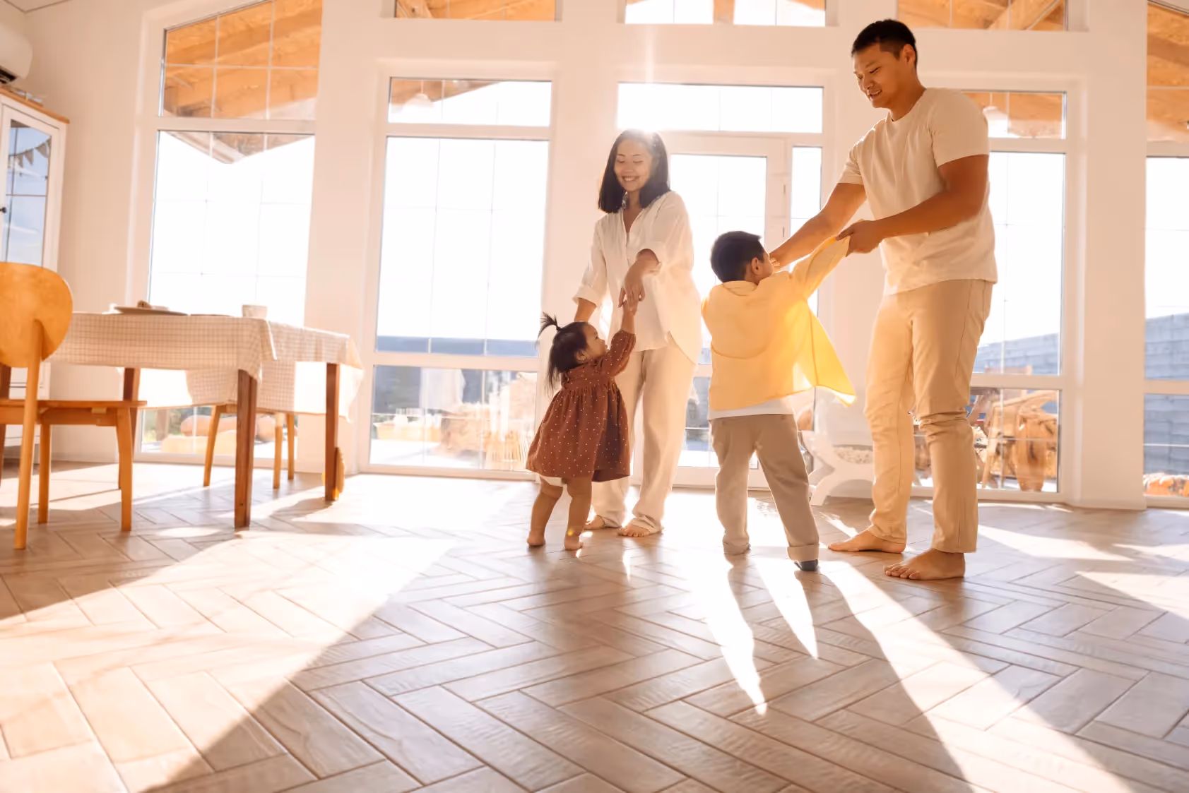 Happy family of four (two adults, two young children) dancing and playing together in a bright, sunlit room, depicting joyful home life at Liberty at Estrella Falls in Goodyear, AZ.