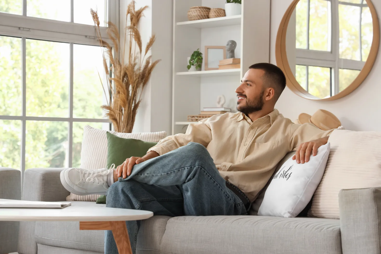 Man relaxing comfortably on a sofa in a bright living room with large windows, showcasing the inviting interiors at Liberty at Estrella Falls in Goodyear, AZ.