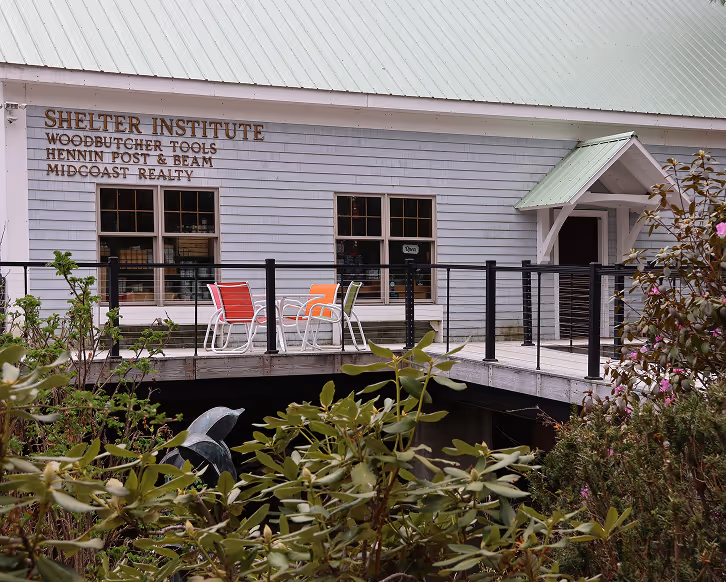 Shelter Institute building with chairs on wooden porch, surrounded by greenery
