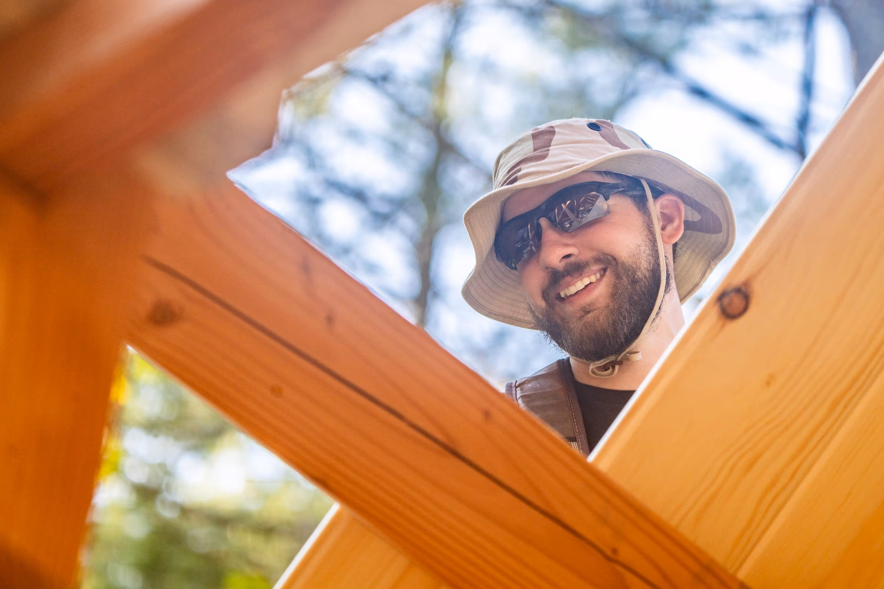 Smiling person in sunhat and sunglasses viewed through wooden frame outdoors