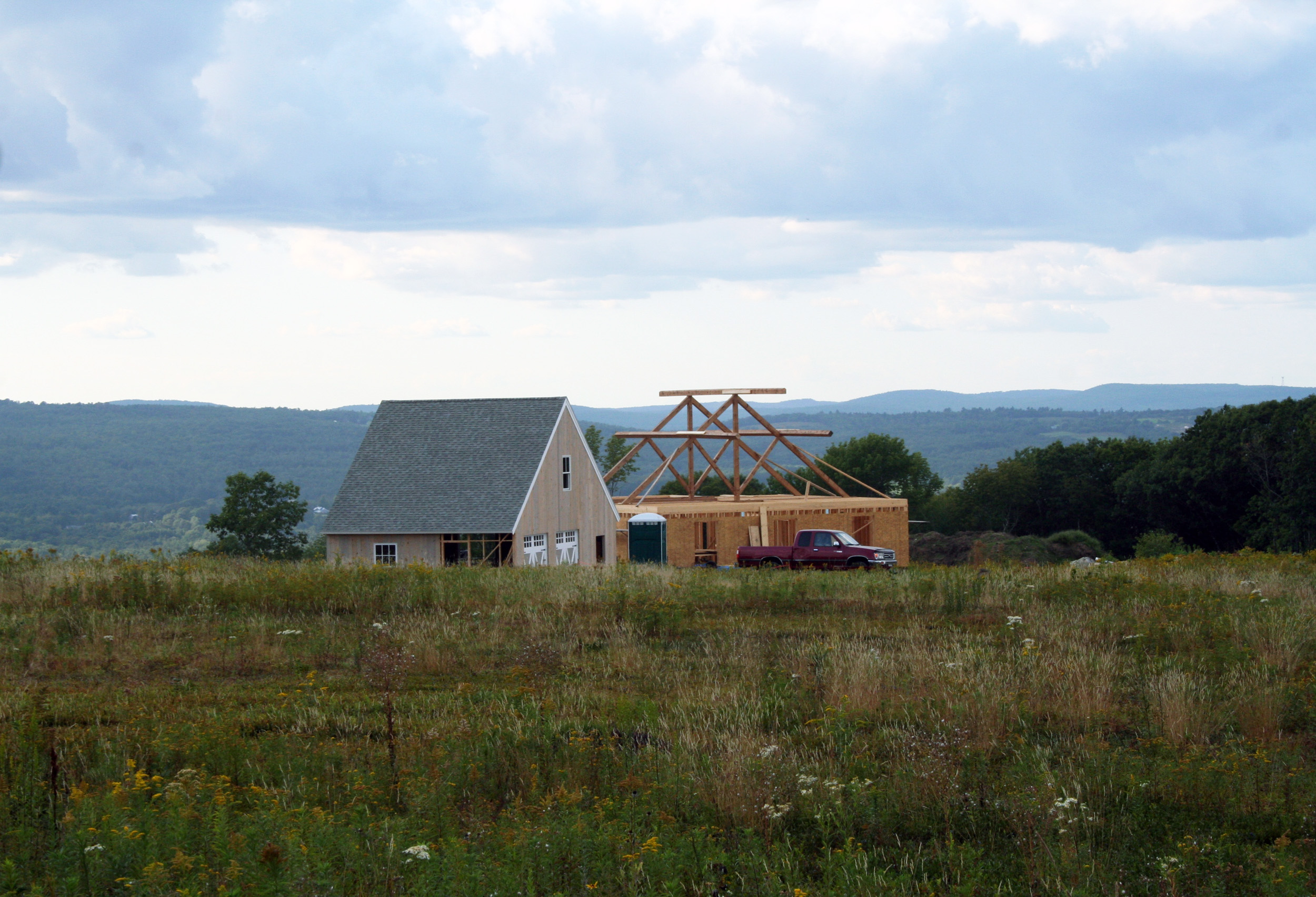 House under construction in rural field with mountains and cloudy sky
