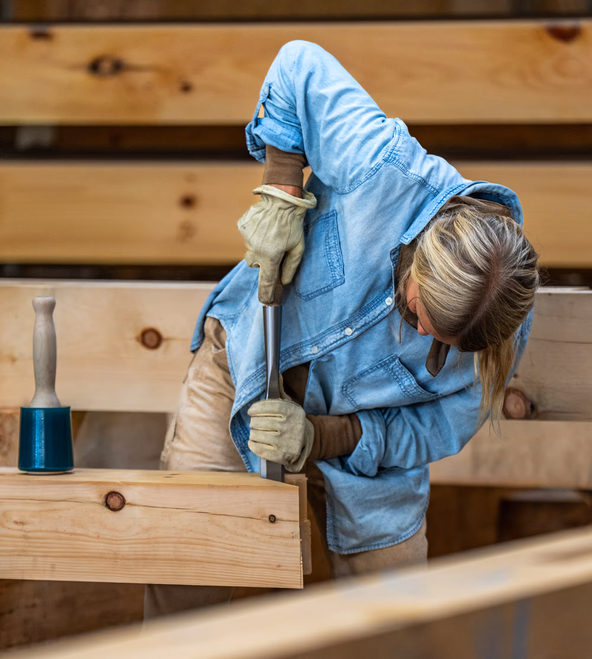 Craftsperson working with wood, wearing denim and leather gloves
