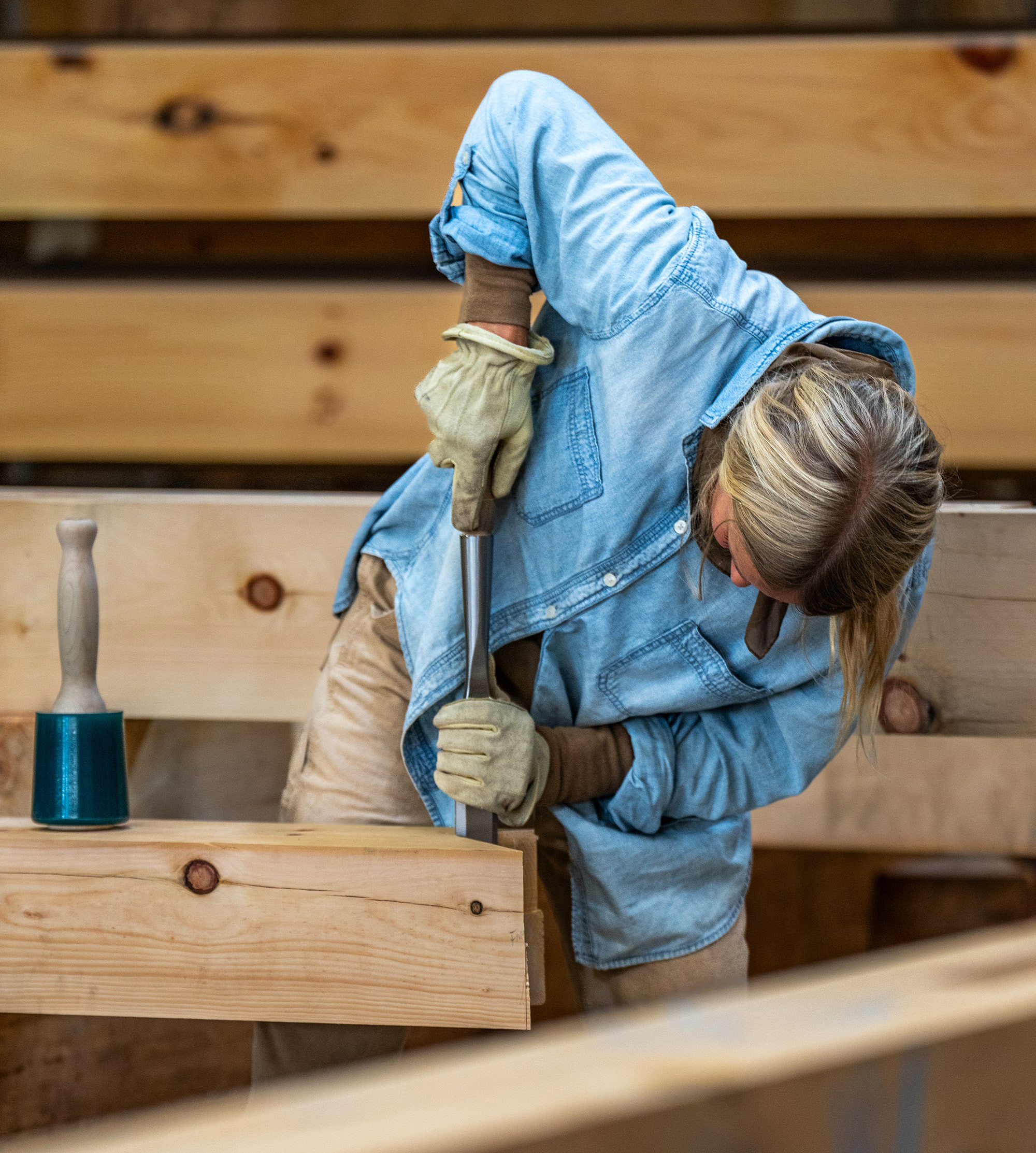 Craftsperson working with wood, wearing denim and leather gloves