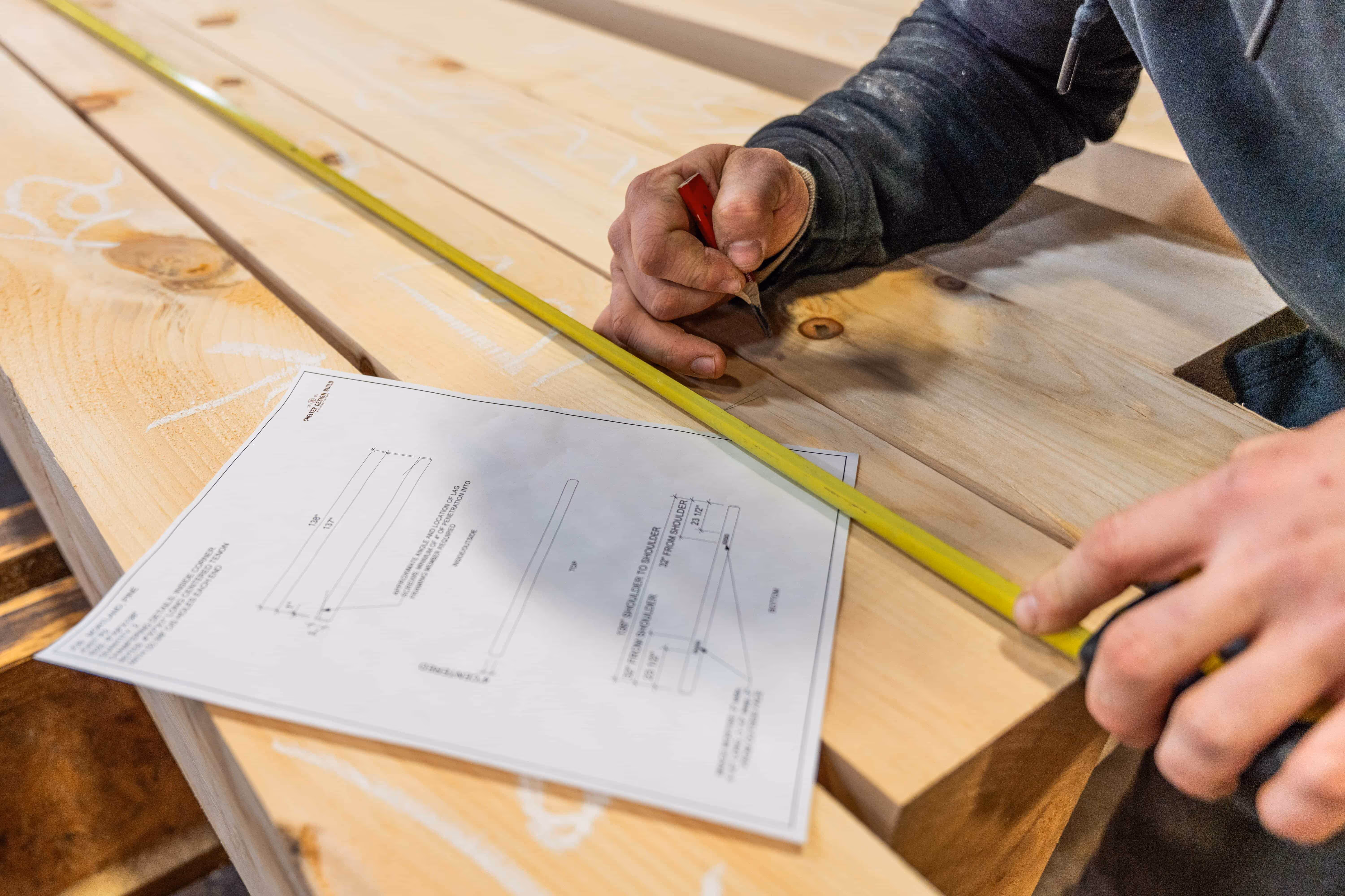 Carpenter measuring wooden plank with yellow tape measure and marking document