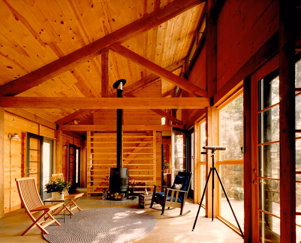 Cozy wooden cabin interior with wood stove, rocking chair, and large windows