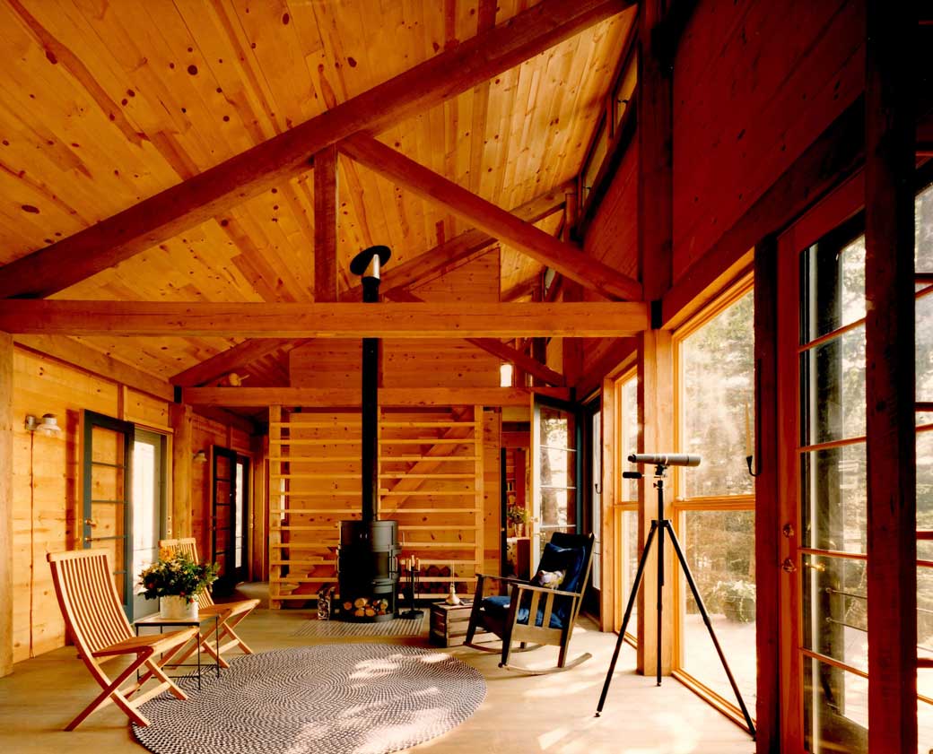 Cozy wooden cabin interior with wood stove, rocking chair, and large windows