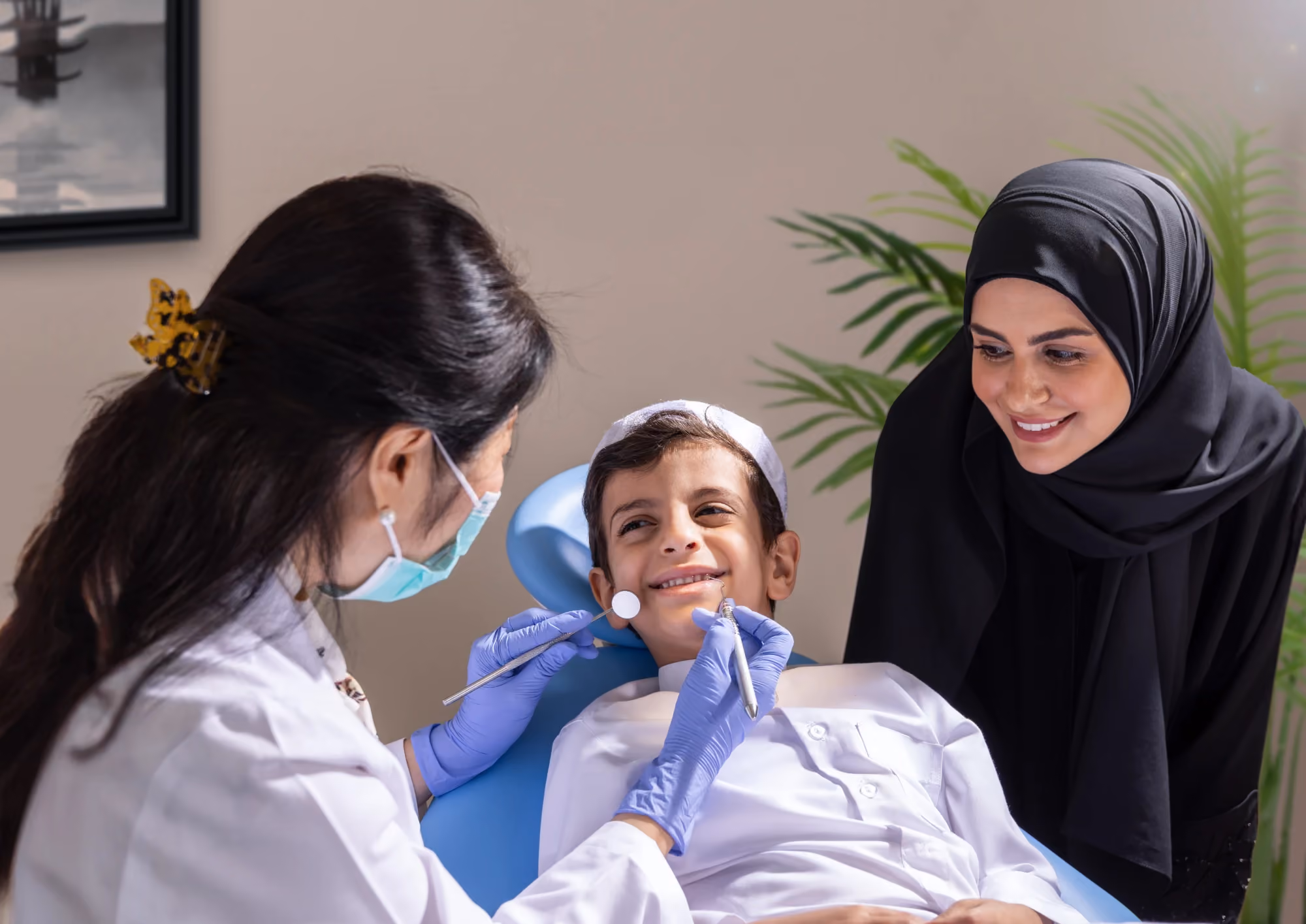 Dentist treating a smiling young boy while his mother sits beside him at KMC