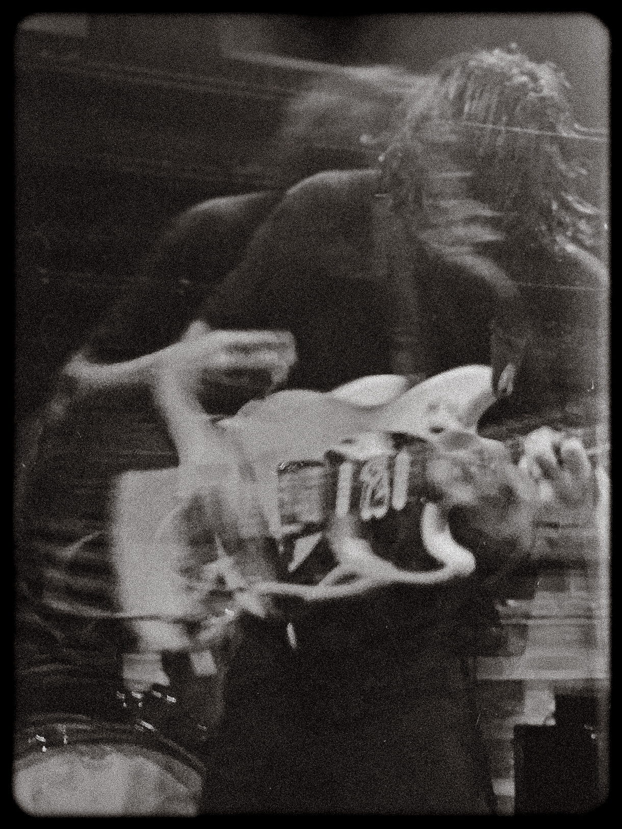 Black-and-white blurred photo of a person playing an electric guitar with visible motion.