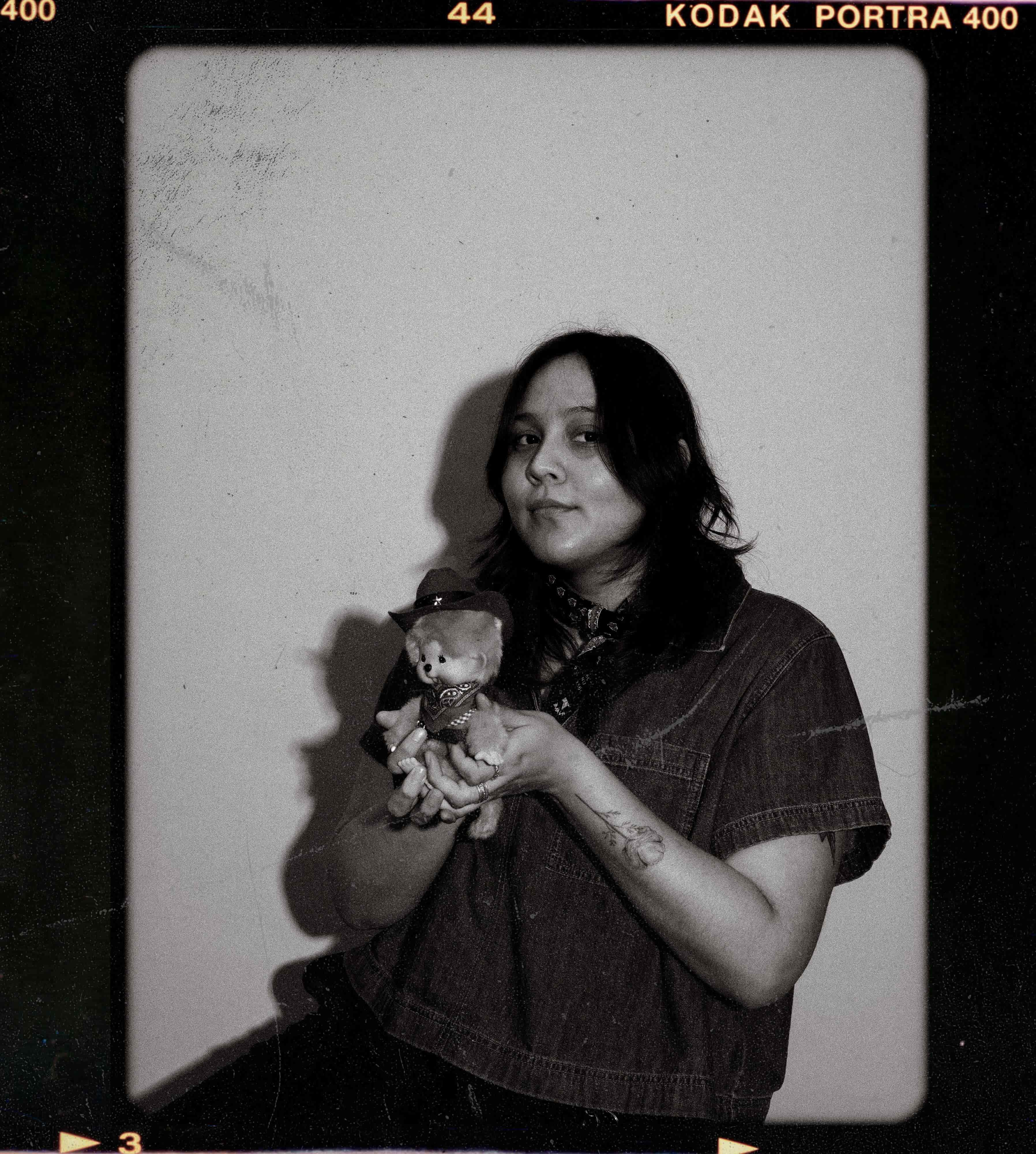 Black-and-white film strip style photo with two portraits of a person with shoulder-length hair, resting their chin on their hand, looking to the side and upward against a curtain background.