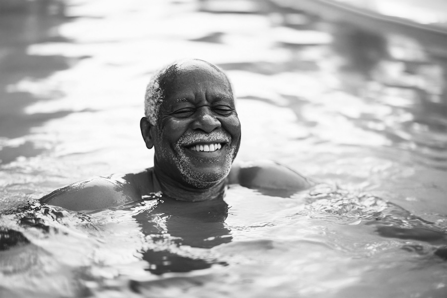Smiling older man swimming in a pool with water up to his shoulders, black and white
