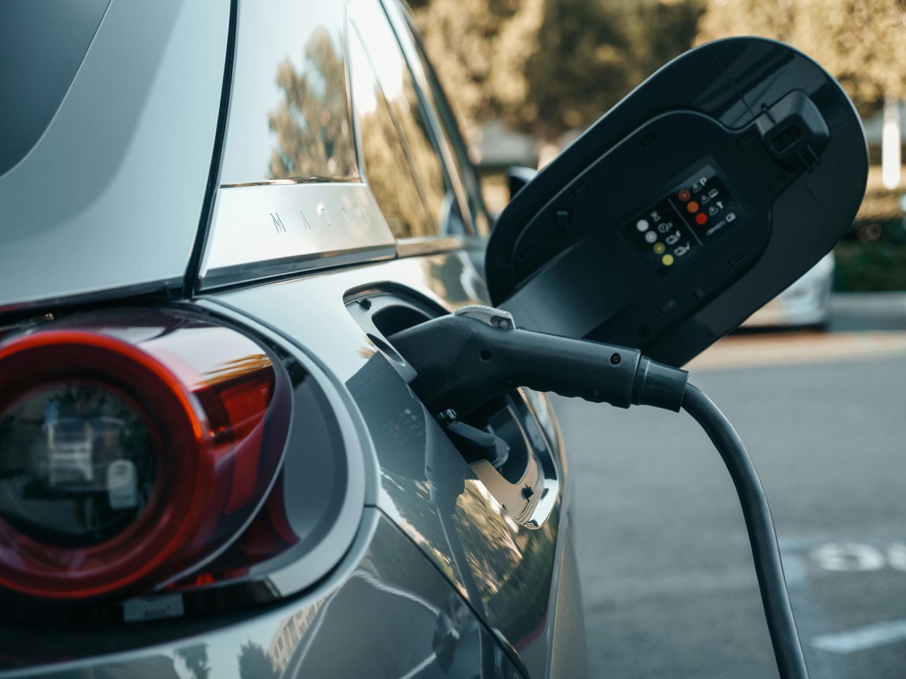 A closeup of a grey car with an EV charger plugged in