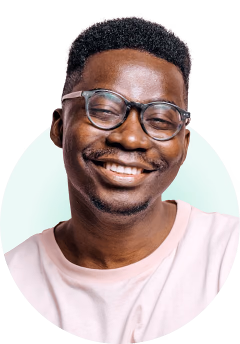 Smiling man with glasses and short curly hair wearing a light pink shirt.