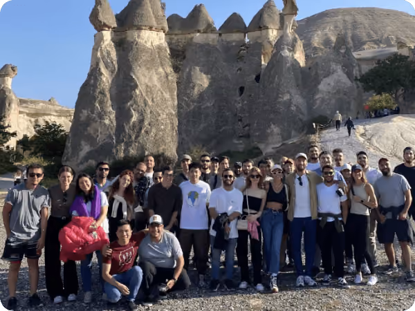 Group of people posing outdoors in front of unique, tall rock formations under a clear blue sky.