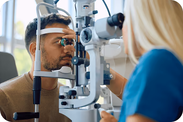 A man undergoing an eye examination using a slit lamp by a healthcare professional in a clinical setting.