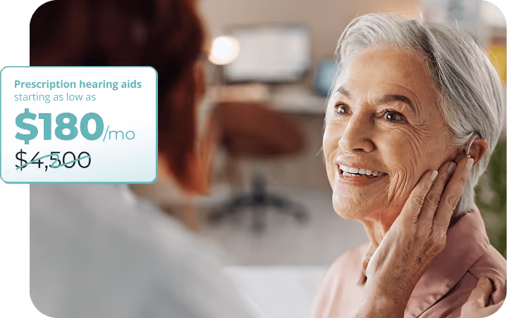 Smiling elderly woman with gray hair touching a hearing aid in her ear, facing another person in a consultation setting, with an overlay text showing a discounted price for prescription hearing aids starting at $180 per month from an original $4,500.