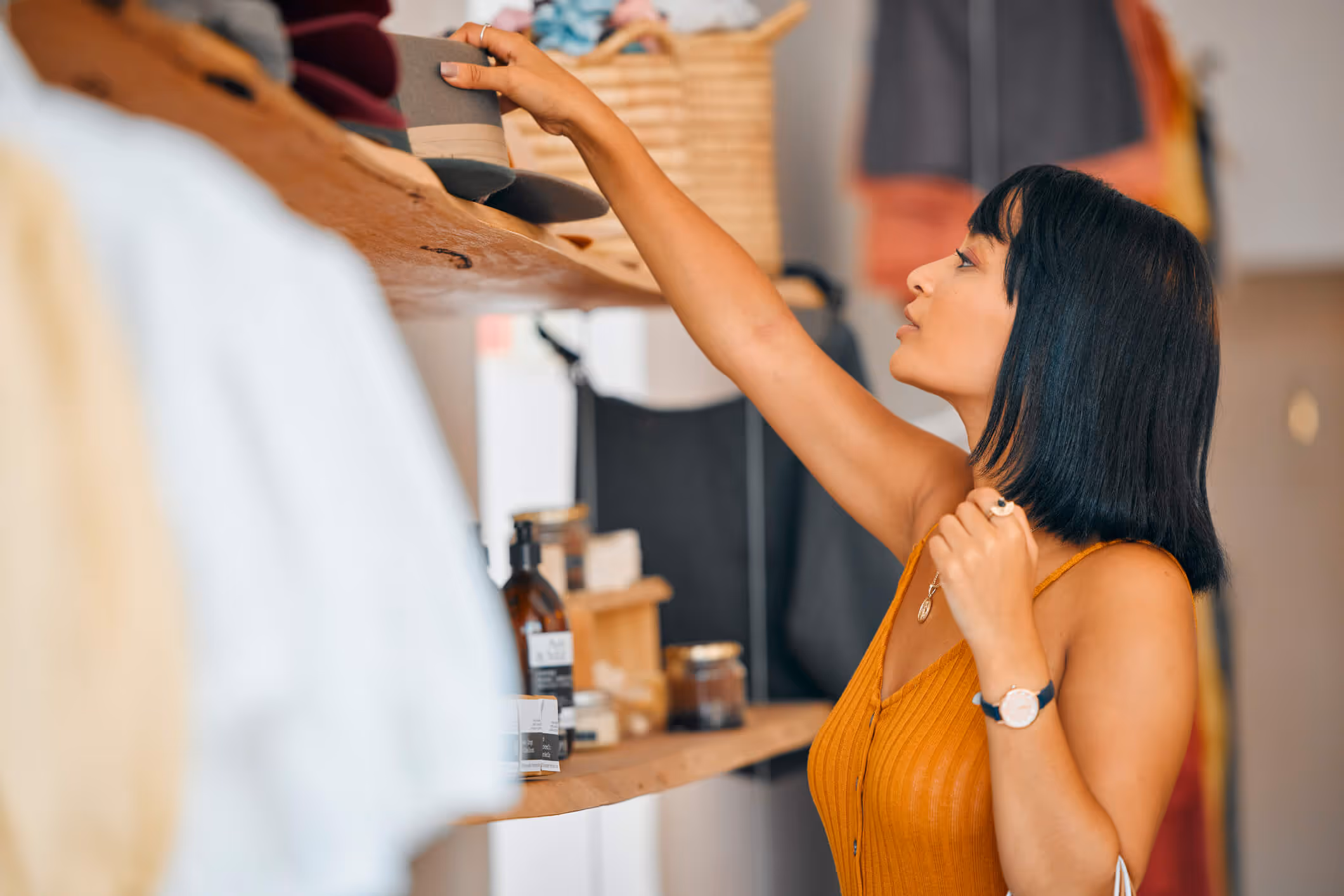 Woman reaching to pick a gray hat from a wooden shelf in a boutique store.