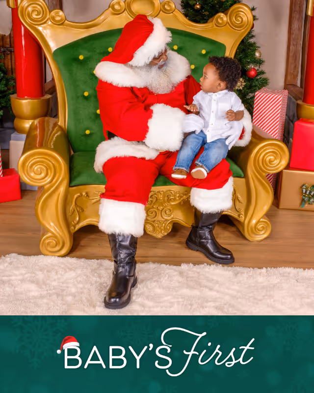 Black Santa Claus in red suit holding a baby on a green and gold chair with Christmas decorations and presents in the background, with text 'Baby's First'.