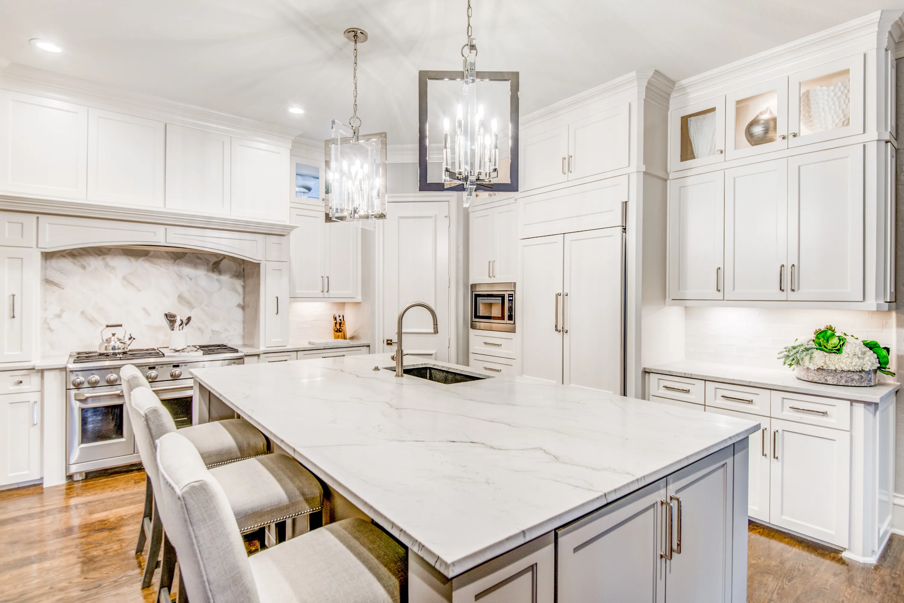 Bright white remodeled kitchen with a large marble-look island and crystal pendant lights