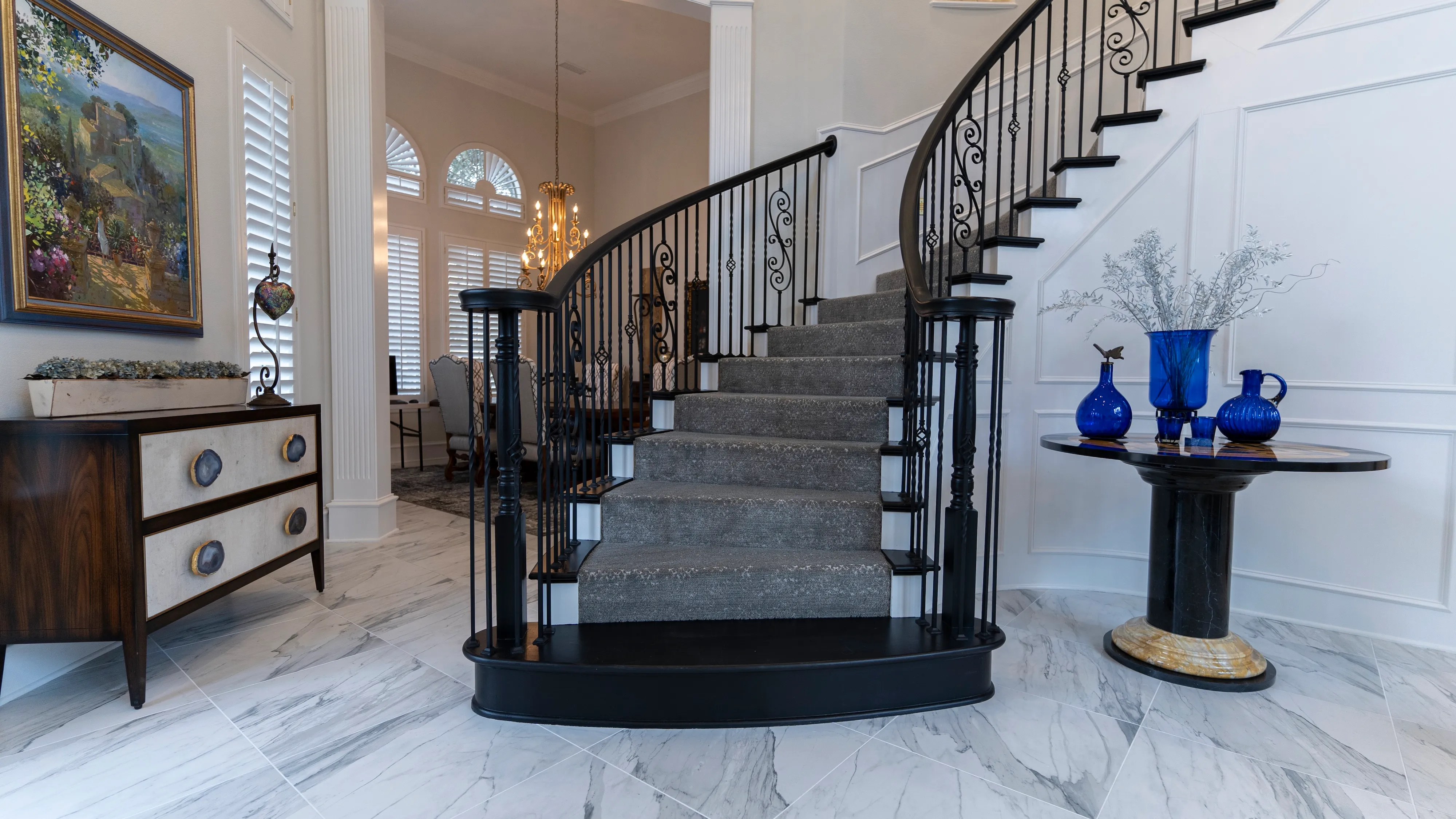 Curved staircase with a fitted gray carpet runner, black railings, and marble foyer floor