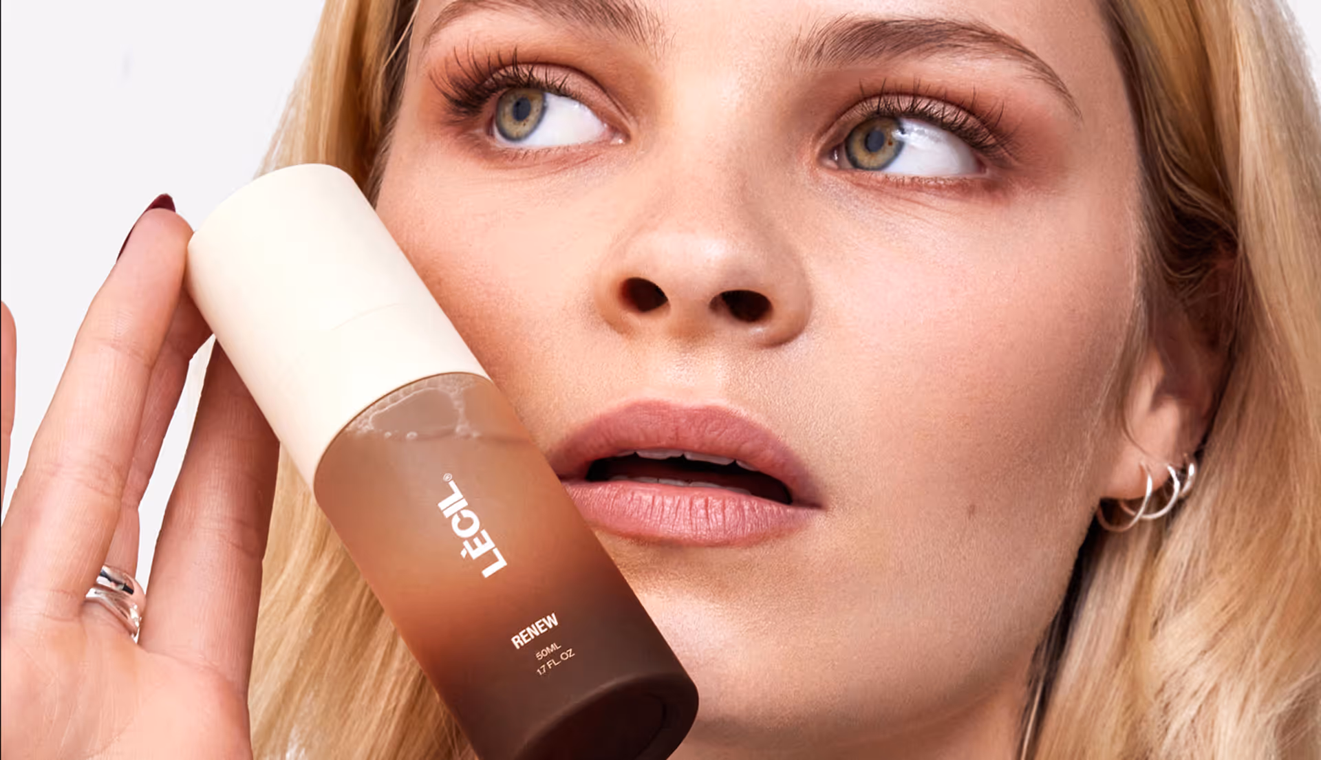 Close-up of woman holding LECIL Renew skincare serum bottle near her face.