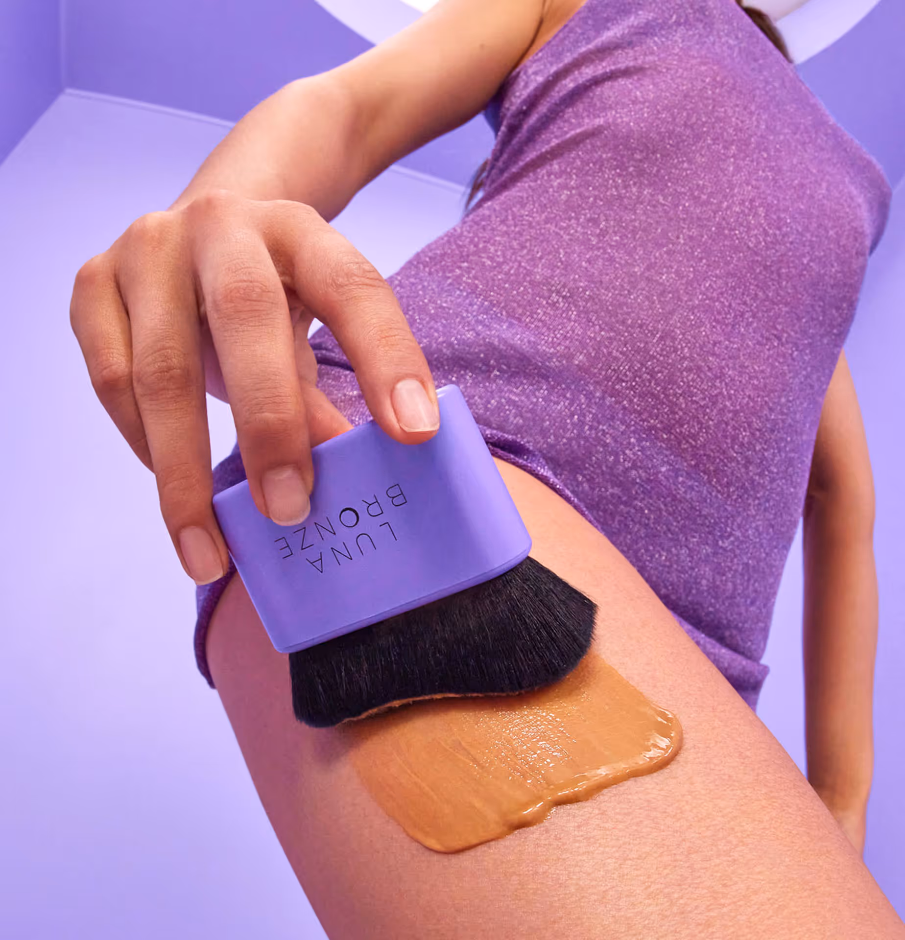 Person applying Luna Bronze self-tanning product on thigh with purple applicator brush.