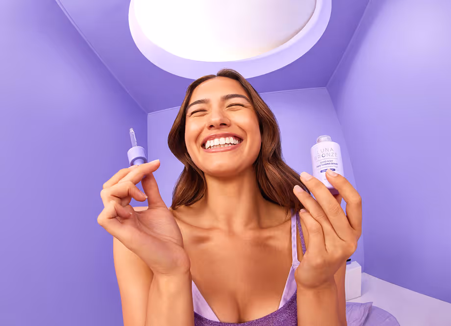 Smiling woman holding a purple serum bottle and dropper in a purple room under a circular light.