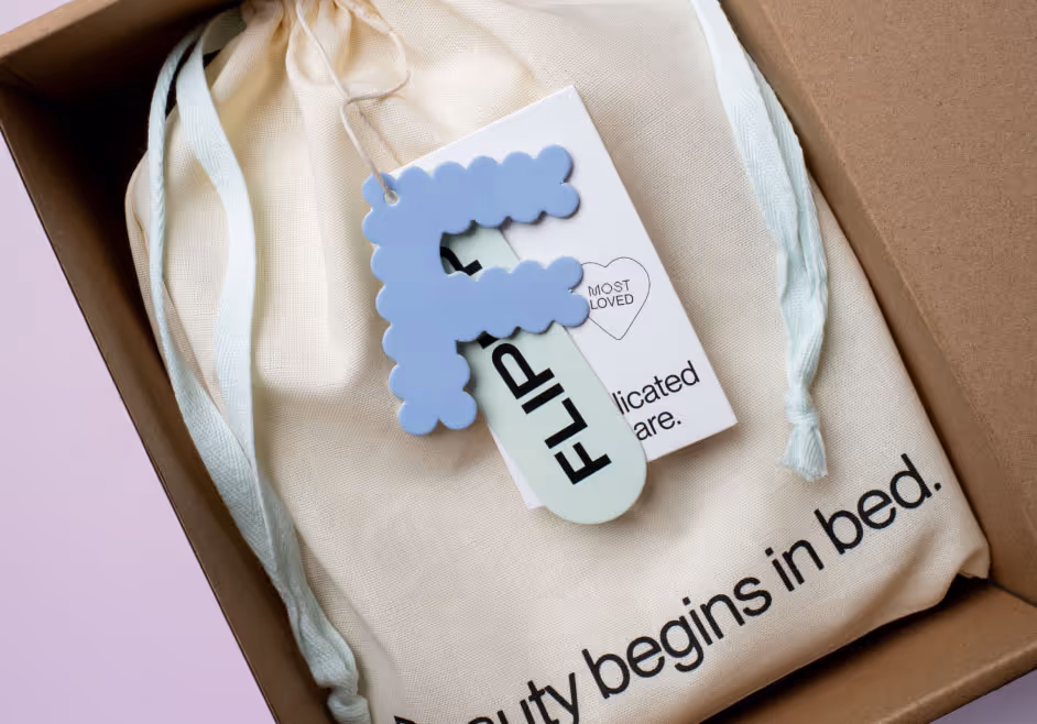 Box with cloth bag labeled 'Beauty begins in bed' and a blue letter F keychain tagged FLIP.
