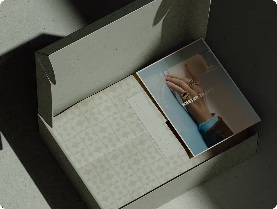 Open box with patterned tissue paper and a booklet featuring a hand wearing rings on a blue sleeve.