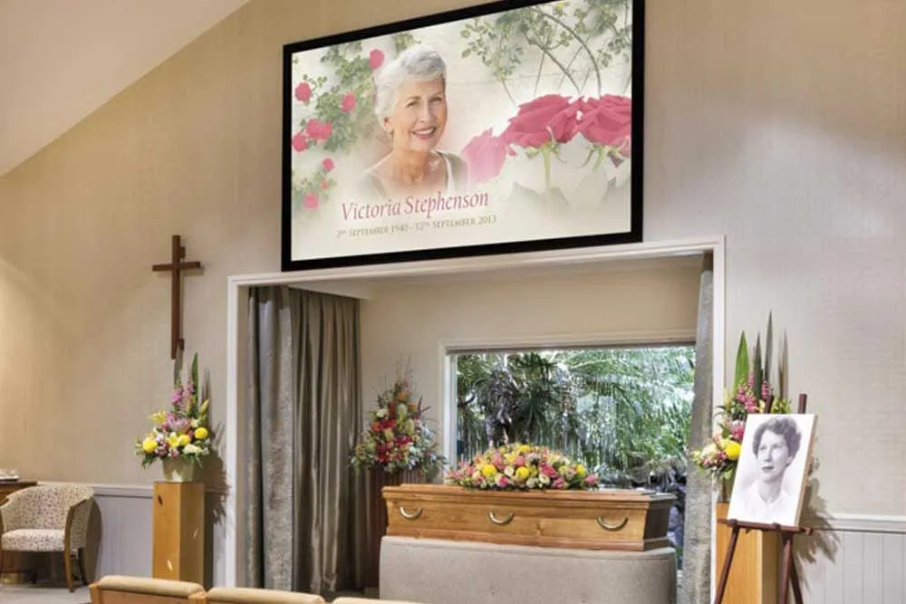 Chapel with coffin, flowers, and a large memorial screen.