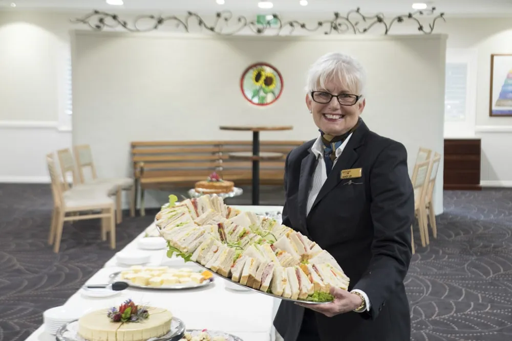Server standing behind a buffet table with food.