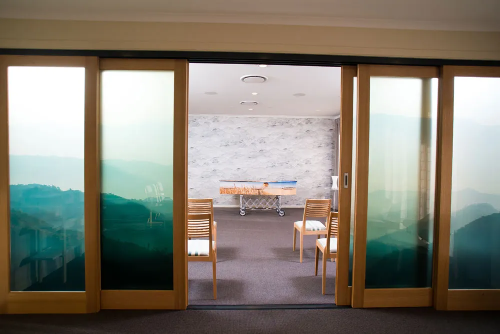 Viewing room with coffin and chairs, seen through sliding doors.