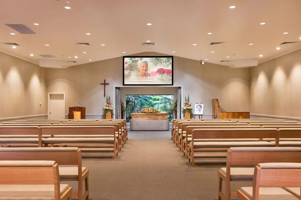 Chapel with pews, screen showing a woman, and coffin.