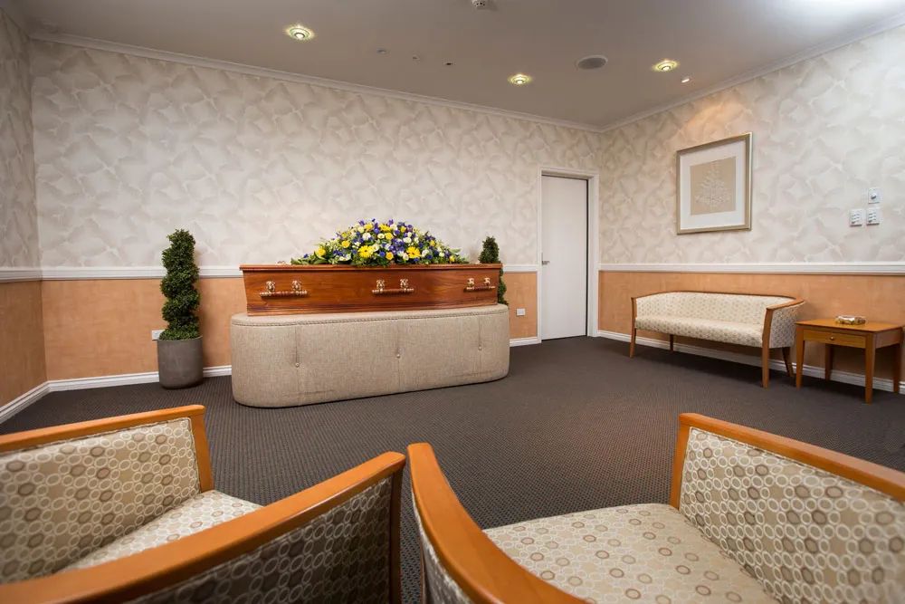 Coffin with flowers in a viewing room with seating.